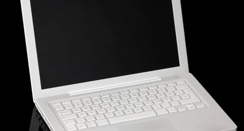 Hvid computer på sort baggrund En hvid bærbar computer med en sort skærm står på en blank overflade mod en sort baggrund.